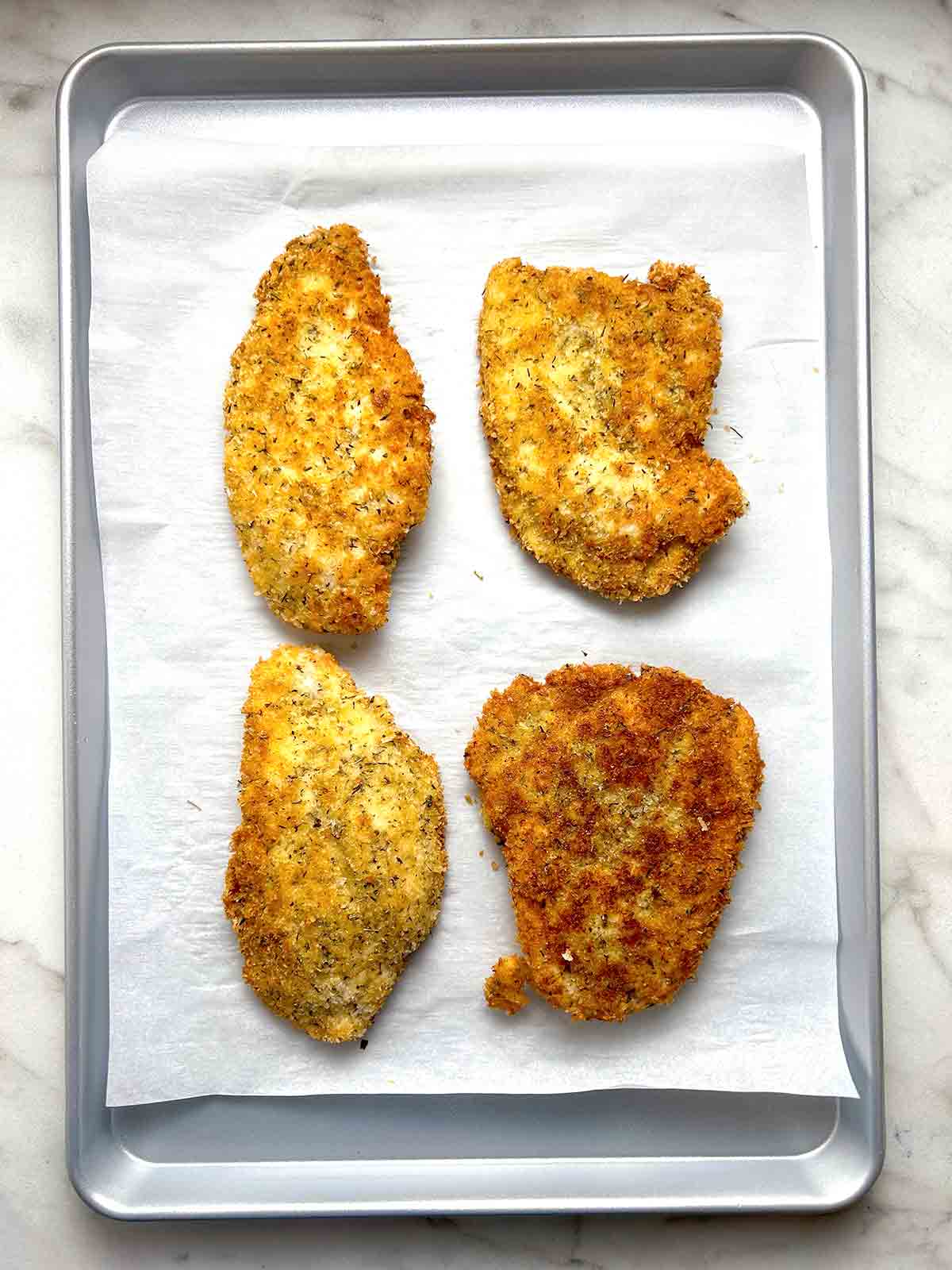 4 pieces of breaded chicken placed on parchment-lined baking sheet.