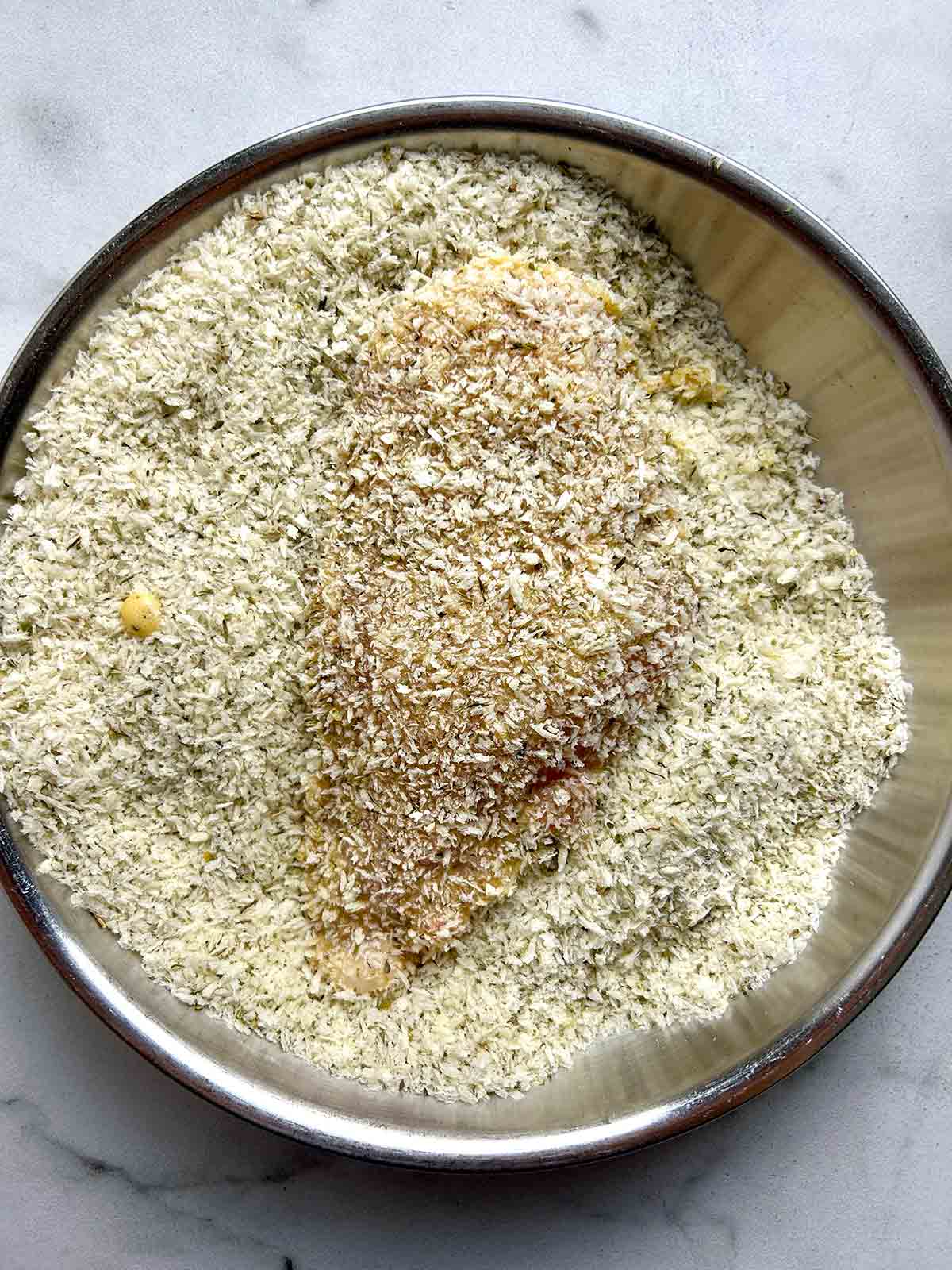 chicken cutlet coated in breadcrumbs in shallow dish.
