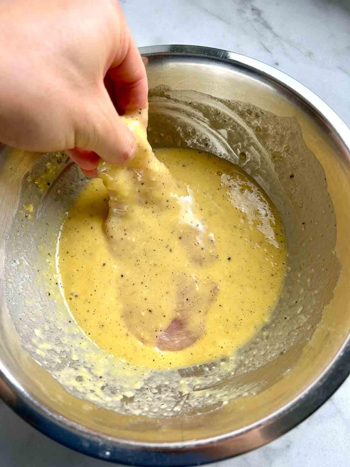 chicken cutlet being dredged in egg wash.