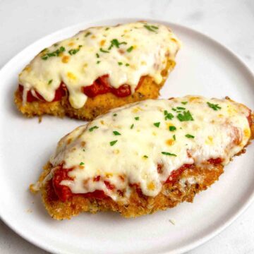 close up of two pieces of chicken parmesan garnished with parsley.