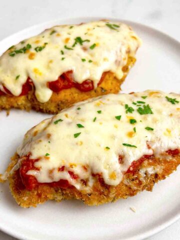 close up of two pieces of chicken parmesan garnished with parsley.