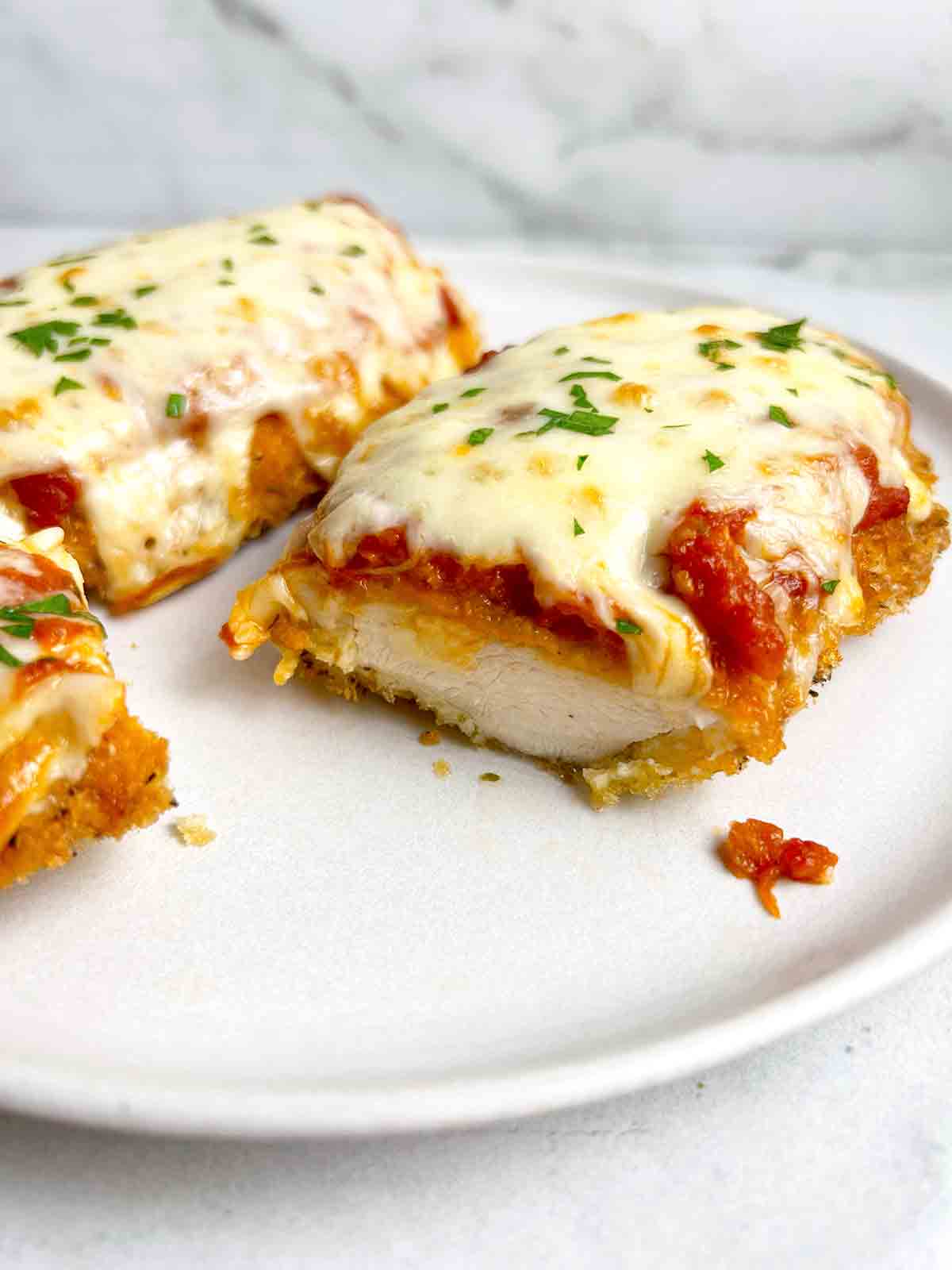 close up of plate of two pieces of chicken parmesan; one is cut in half to show the inside.