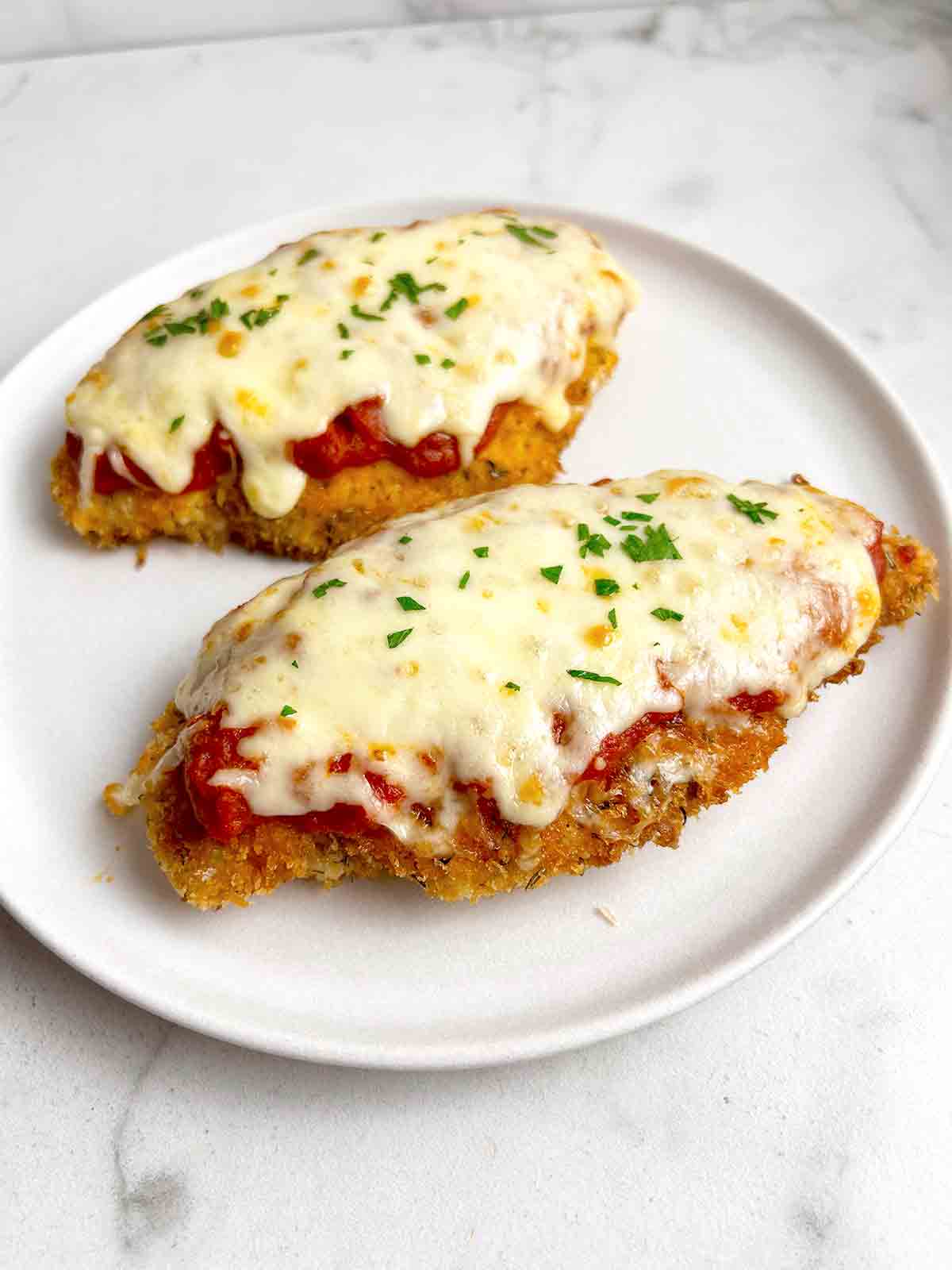 close up of two pieces of chicken parmesan garnished with parsley.