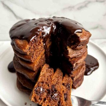 stack of chocolate pancakes with section cut through middle; chocolate sauce running down from top of stack.