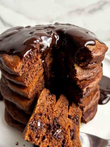 stack of chocolate pancakes with section cut through middle; chocolate sauce running down from top of stack.