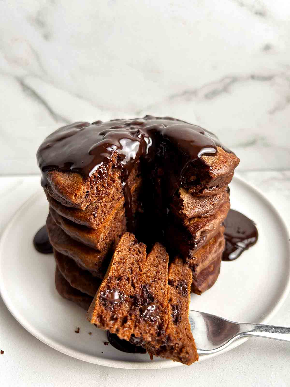 stack of chocolate pancakes with section cut through middle; chocolate sauce running down from top of stack.