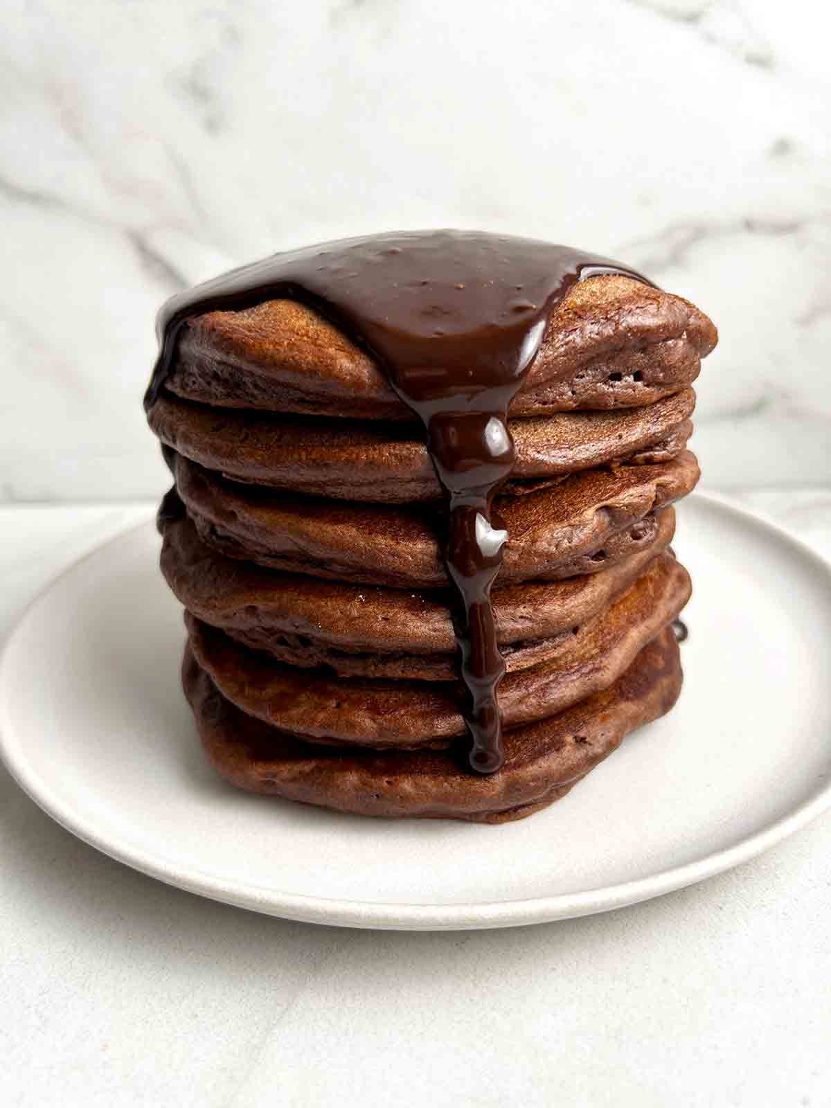 stack of chocolate pancakes with chocolate sauce poured over top.