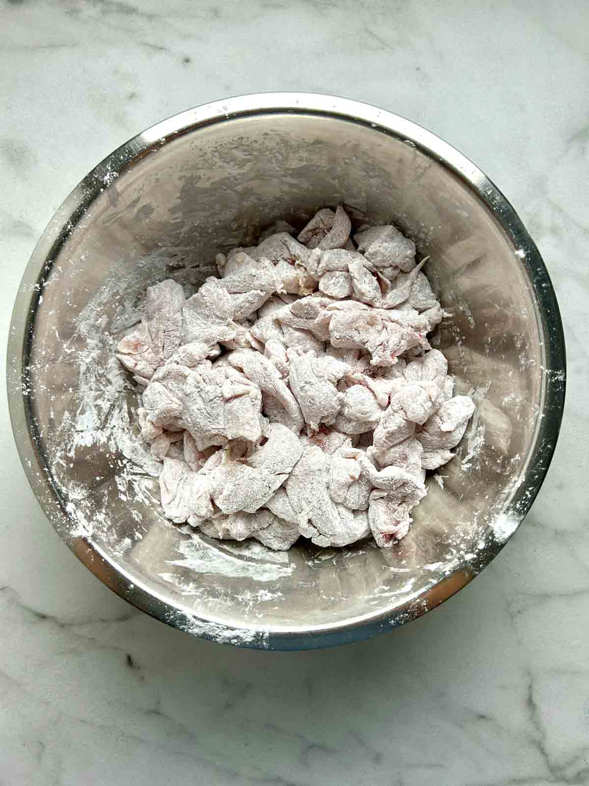 chicken pieces coated in cornstarch in bowl.