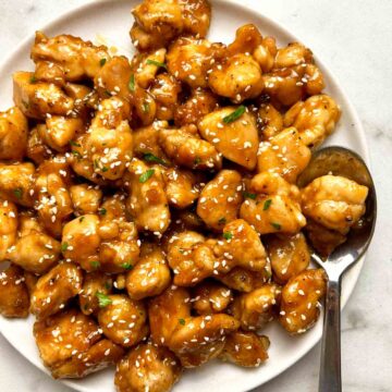 close up of honey garlic chicken bites on plate; spoon on side of plate.
