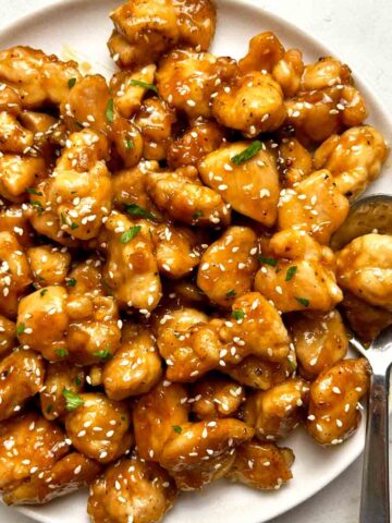 close up of honey garlic chicken bites on plate; spoon on side of plate.