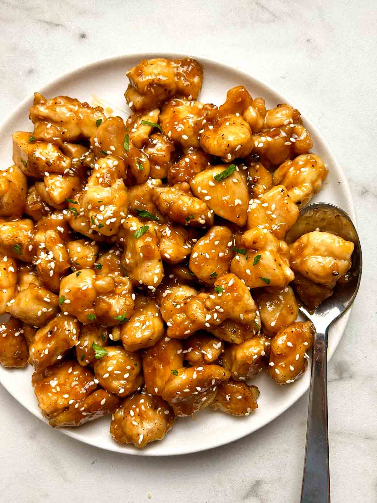 close up of honey garlic chicken bites on plate; spoon on side of plate.