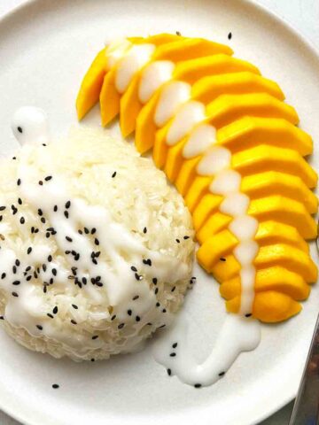 close up of mango stick rice on plate with fork. Black sesame seeds for garnish.