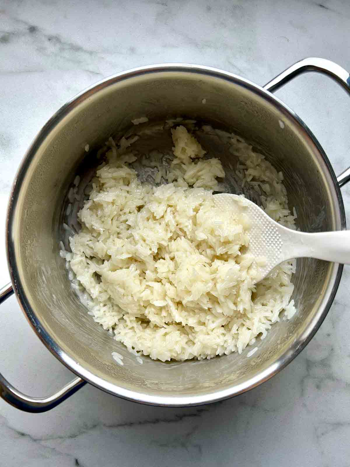 cooked sticky rice tossed with coconut sauce in medium pot.