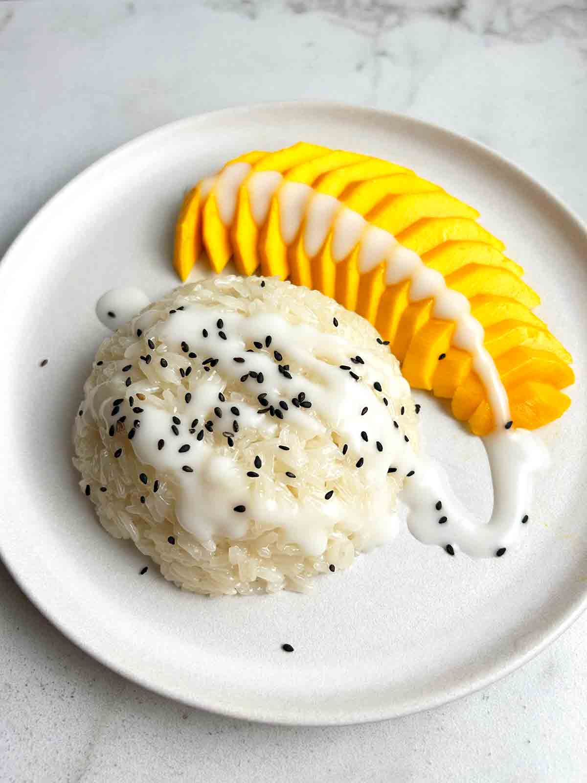 close up of mango stick rice on plate with fork. Black sesame seeds for garnish.