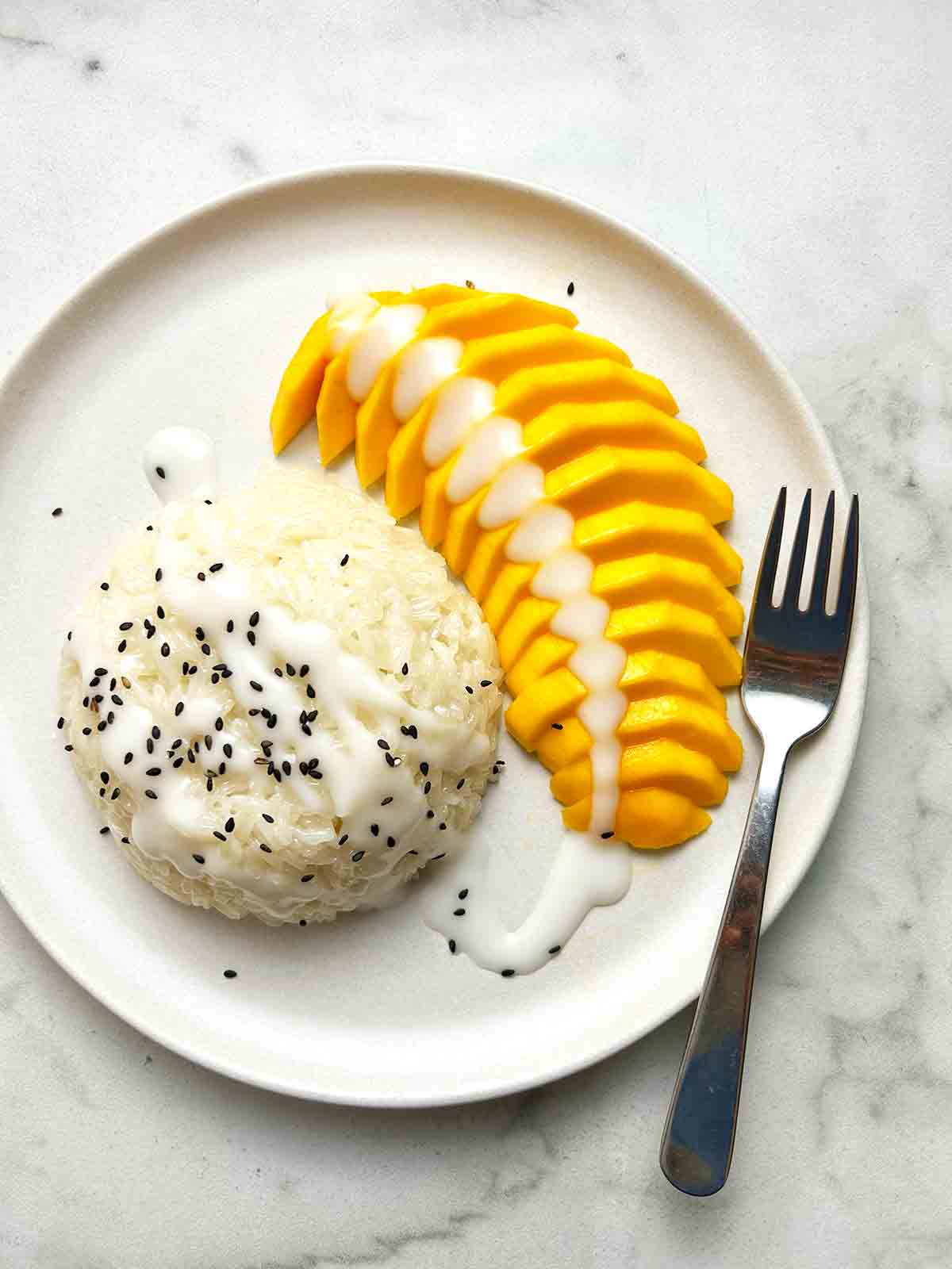 close up of mango stick rice on plate with fork. Black sesame seeds for garnish.