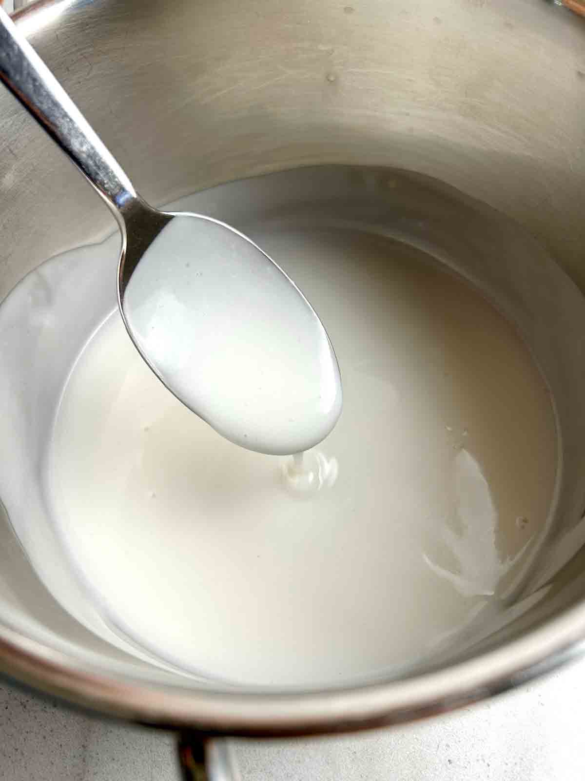 spoon lifting smooth coconut sauce from saucepan.