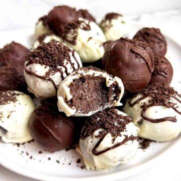 close up of plate of Oreo balls; one has a bite taken out of it to show the inside.