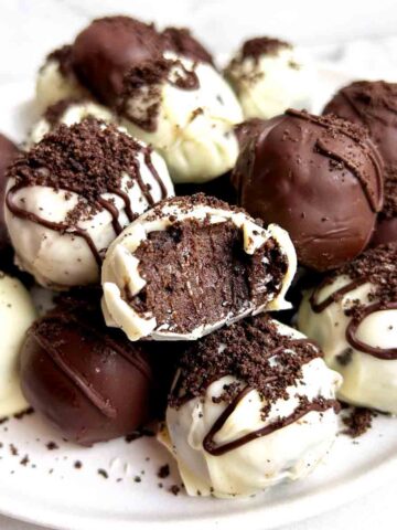 close up of plate of Oreo balls; one has a bite taken out of it to show the inside.