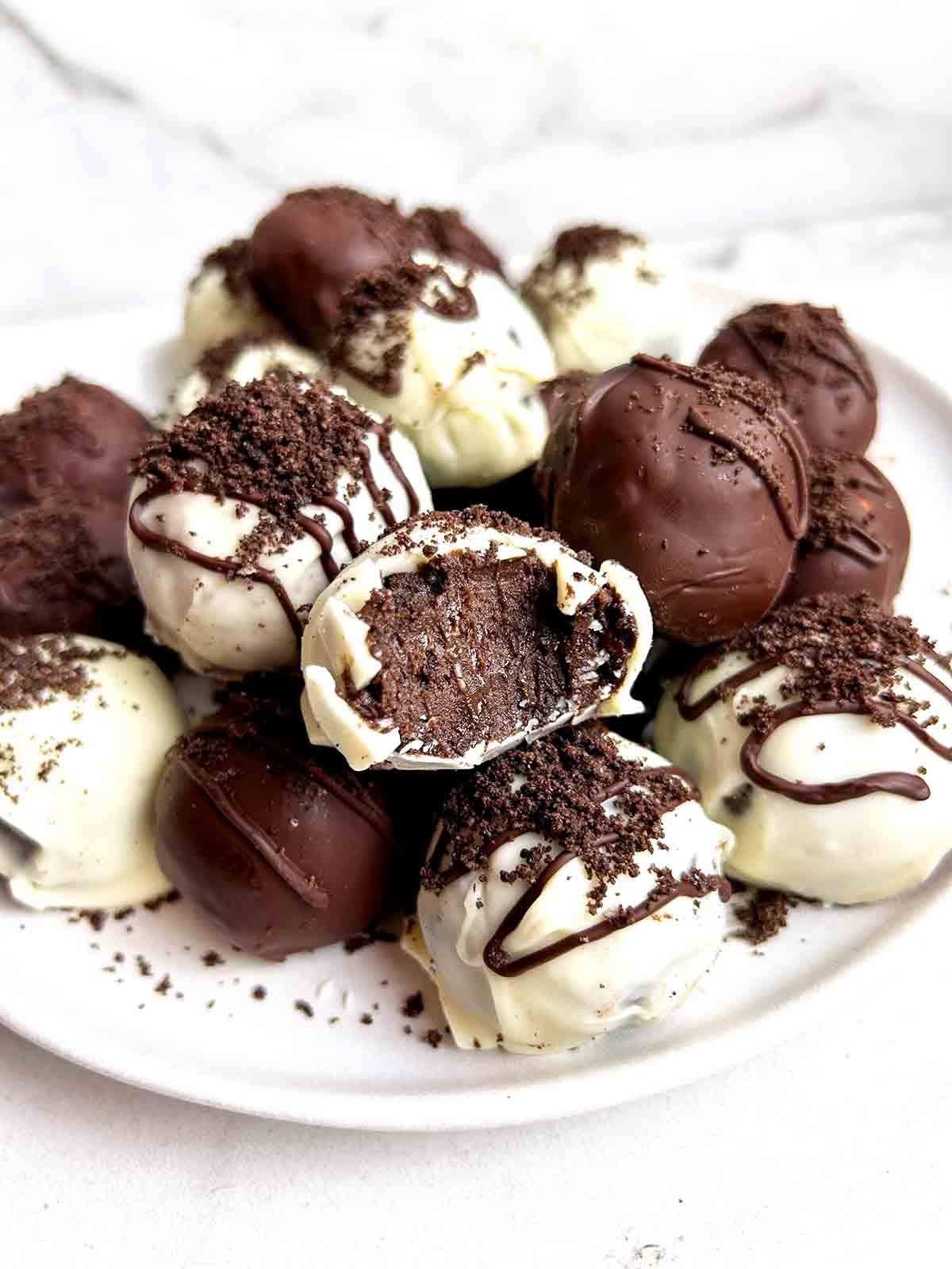 close up of plate of Oreo balls; one has a bite taken out of it to show the inside.